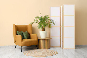 Interior of room with folding screen, armchair and houseplant near beige wall
