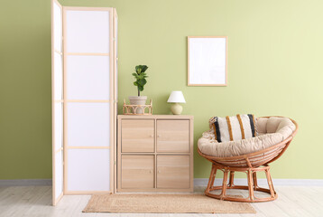 Interior of room with folding screen, commode and armchair near green wall