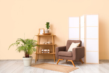 Interior of room with folding screen, armchair and shelving unit near beige wall