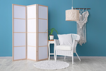 Interior of room with folding screen, wicker chair and home decor near blue wall
