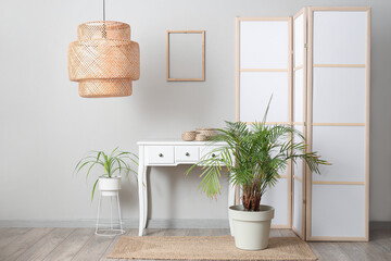 Interior of room with folding screen, commode and houseplants near white wall