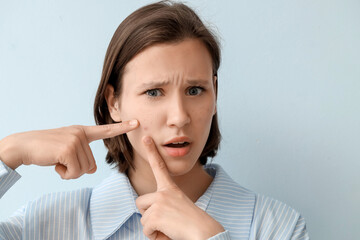 Beautiful young woman with acne problem squishing pimples on blue background