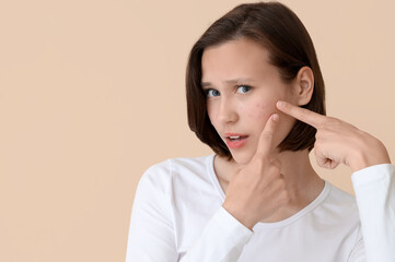 Beautiful young woman with acne problem squishing pimples on beige background