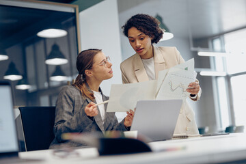 Female boss discussing project with employee showing presentation to team leader