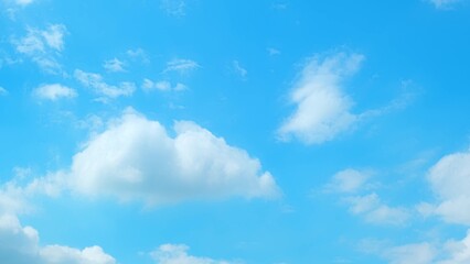 A clear blue sky with a few scattered fluffy white clouds. The clouds are soft and puffy, floating...