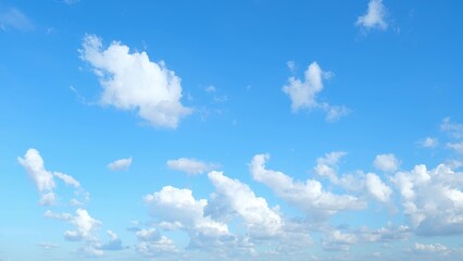 A bright blue sky dotted with numerous fluffy white clouds. The clouds are scattered across the...