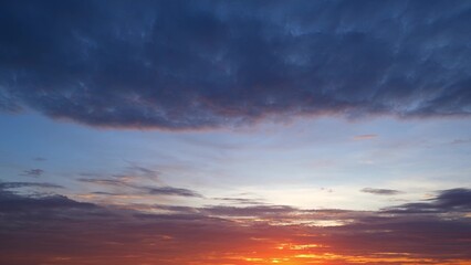 Obraz premium A stunning sunrise with a vibrant orange and red horizon. Above, the sky transitions into shades of blue and purple, with a mix of dark and light clouds creating a dramatic effect. 