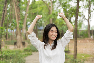 Portrait of asian woman breathing fresh air in a forest.Carefree asian girl smiling and enjoying summer sunny day in park.Young woman arms raised enjoying the fresh air in green park.