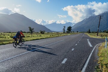 Cyclists on country road leading into the Southern Alp mountain range. Haast, West Coast, New...