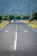 Cyclists on country road leading into the Southern Alp mountain range. Haast, West Coast, New Zealand.