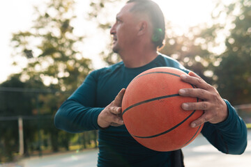 Adult male athlete about 50 years old, practicing basketball in a wheelchair, with a disability, and wearing sports clothing. with detail in the hands and ball, in a park and sunny day