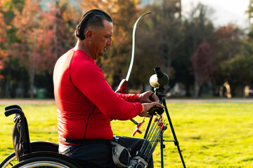 Wheelchair athlete, approximately 50 years old, preparing and practicing archery, with his equipment, bow and arrow, outdoors on a sunny day