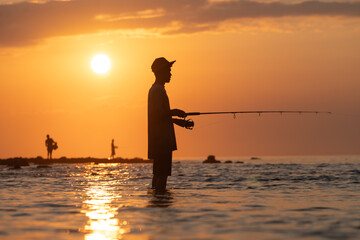 Young male fisherman with hat fishing in the sunset.