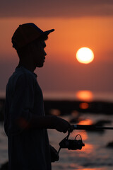 Close up of young fisherman with hat fishing in the sunset.