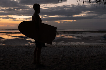 Male surfer with broken surf board under the arm watching the sunset.