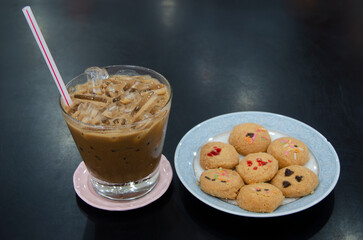 Iced coffee mug and plate of cookies on black background
