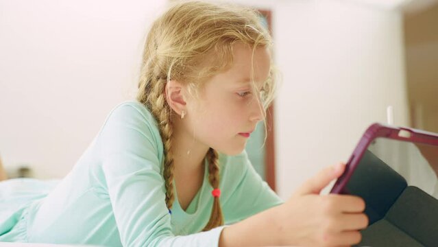 Caucasian young girl using digital tablet learning in bedroom at house.