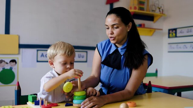 Teacher helping kid with wooden toy at kindergarten school class. Education, smart games for children