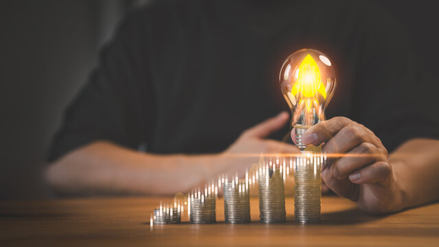 New investor hand holding a light bulb putting on money stack. New ideas for investment, savings money, taxes, retirement, working, small business, finance, investment, startup, and financial concept.