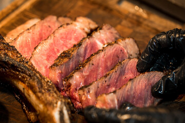 Top view of ultra-thin slices of rare, large roast beef on an Australian tomahawk steak. Revealing pink flesh Beautiful golden brown shell Served on a black butcher knife on the table, yes.