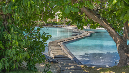 A pedestrian winding concrete path crosses the turquoise swimming pool. The cottage is far away. In...