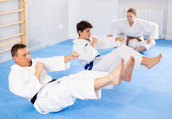Obraz premium Woman and men in kimono train abdominal muscles and do punches at the same time during karate or judo training