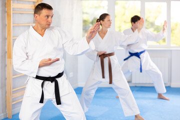 Woman and man in kimono standing in fight stance during group karate training