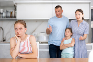 Offended teen girl feeling sad in home kitchen, listening to reprimand of displeased mother and...