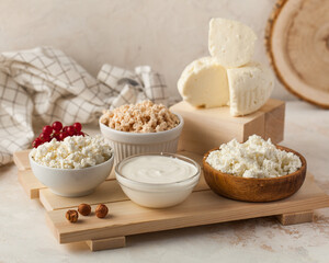 Assorted dairy products including cottage cheese and sour cream on a wooden board. Dairy product