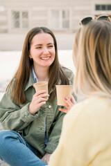 Friends drinking coffee in paper cup while sitting in the street