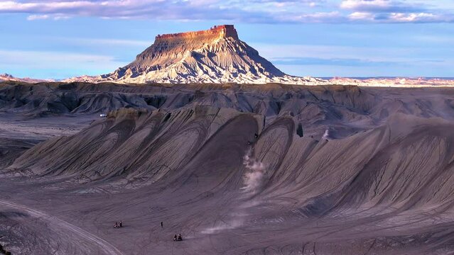 Aerial: Drone Forward Shot Of Men Driving Motorbikes Near Factory Butte Mountain Peak Under Cloudy Sky - Moab, Utah