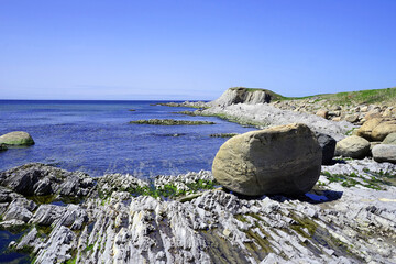 Outcrop by the seaside with a boulder in the foreground and a rocky point in the distance