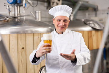 Portrait of brewer who is standing with glass of beer on his workplace in the brew-house