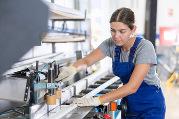 Experienced young female technician, wearing blue overalls and gloves, skillfully operating profile...