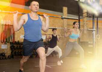 Portrait of sporty man doing exercises with barbell to strengthen body muscles in modern gym during...