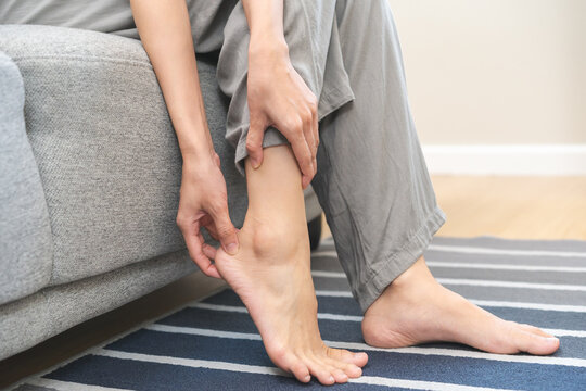 Foot pain concept, close up hand of young woman rubbing, massaging sore feet area of heel, girl suffering on sofa, couch at home. Discomfort painful feet ache from walking for long. Physical injury.