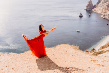 Woman red dress sea. Female dancer posing on a rocky outcrop high above the sea. Girl on the nature...