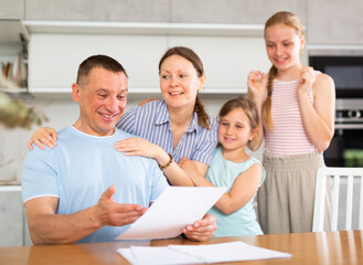 Happy family receiving written notification of positive decision from bank or credit organization about approval of loan or mortgage. Cheerful man with wife and teenage daughters reading some papers