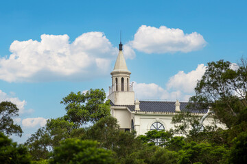 White Church Tower Surrounded by Lush Green Trees under Blue Sky with Fluffy Clouds