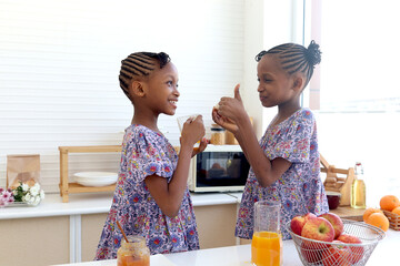 African twin girl sister with curly hair braid African hairstyle drinking orange juice at home...