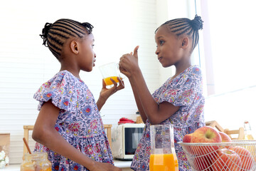 African twin girl sister with curly hair braid African hairstyle drinking orange juice at home...
