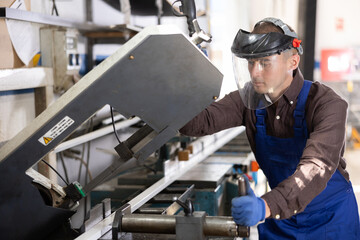 Glass workshop - man works on a machine for cutting aluminum profiles for windows