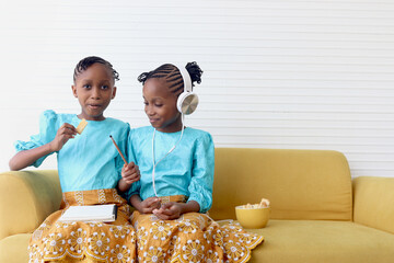 Twin girl sister with curly hair braid African hairstyle do homework, eat snacks, and listen to...