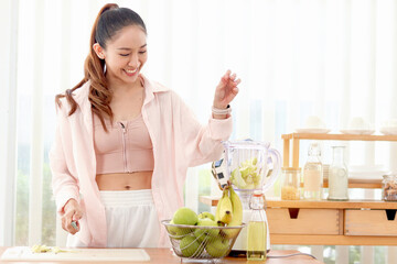 Sporty girl putting mix fruit and vegetable ingredients in blender for making healthy smoothie beverage drink at kitchen. Beautiful happy smiling Asian woman with fruit basket and blender at kitchen.