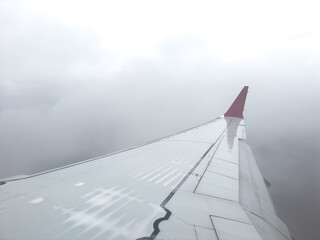 Wing from airplane window on cloudy day. Aerial view of clouds through a plane window. Wing of...