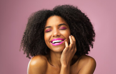 Black woman, makeup and laugh in studio for beauty with cosmetics for skin isolated on pink...