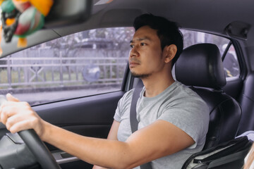 Side view of asian man, bored face, driving a car on road while traveling alone, going to work,...