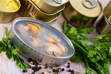 Can of preserves with clams, different closed canned seafoods on background