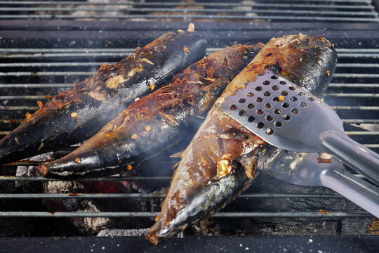 Metallic tongues flipping mackerel fish on grill
