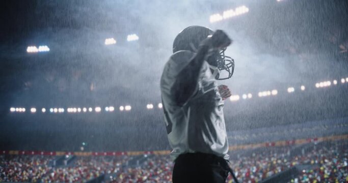 American Football Player Celebrating Championship Win in the Rain on a Floodlit Stadium Field. African Male Athlete Jumping and Punching the Air, Embracing the Moment with Cheering Sports Fans